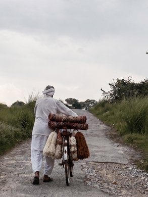 A man walking a bicycle loaded with rolled rugs along a village path