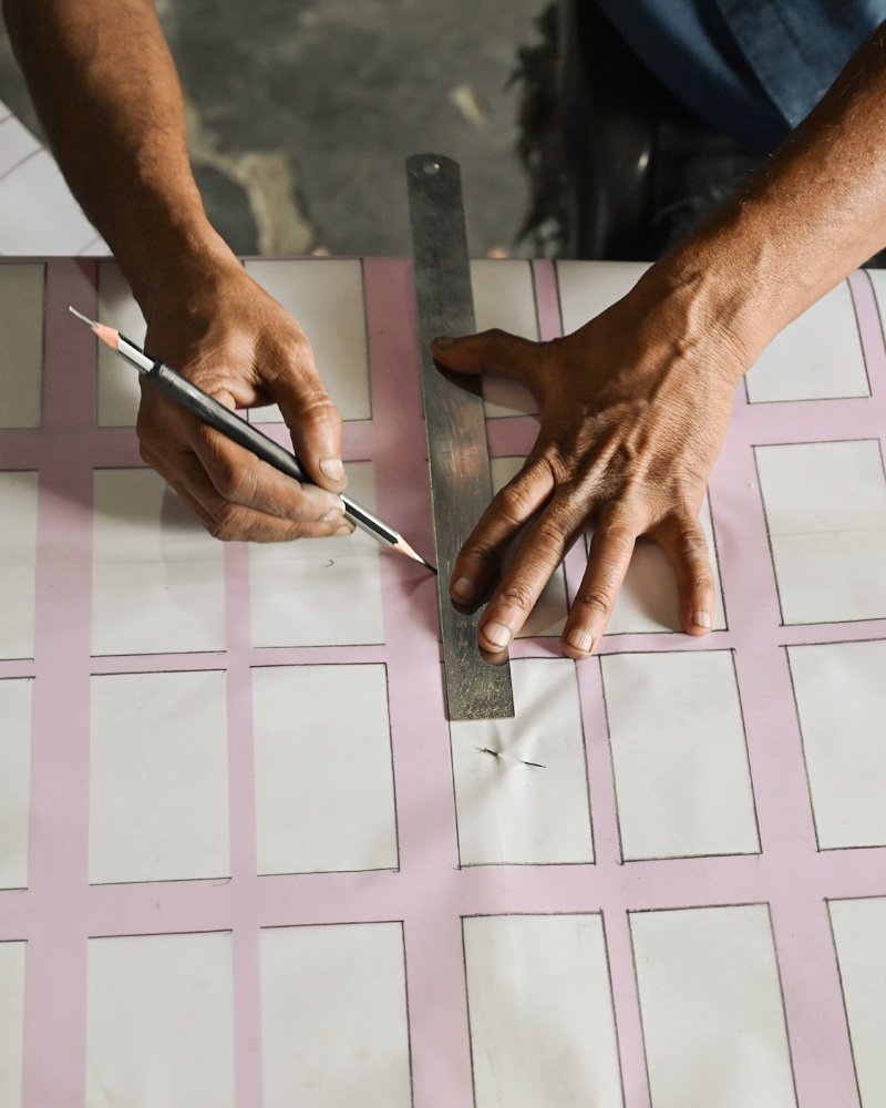 Hands marking out a grid on a rug design template with a pencil and a metal ruler